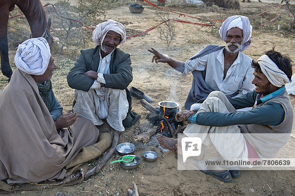Vier Inder mit Turbanen sitzen am Boden und unterhalten sich  auf einem Feuer wird Milchtee zubereitet  Kamelmarkt