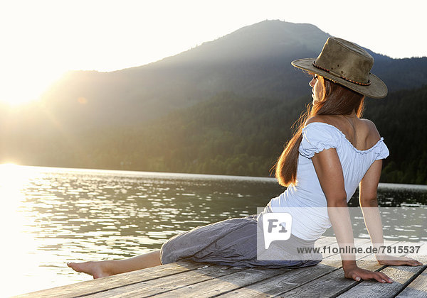 Junge Frau sitzt auf Steg im Sommer