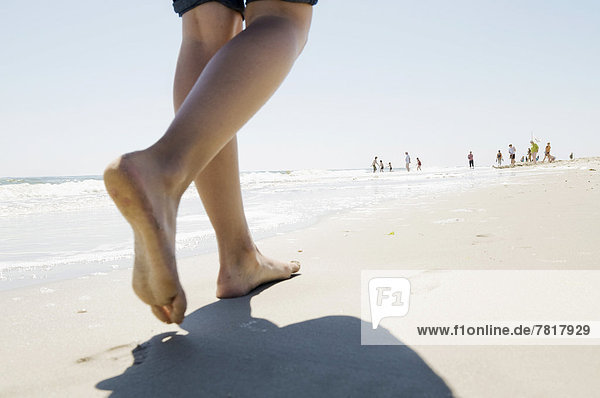 Urlauberin läuft barfuß am Strand entlang