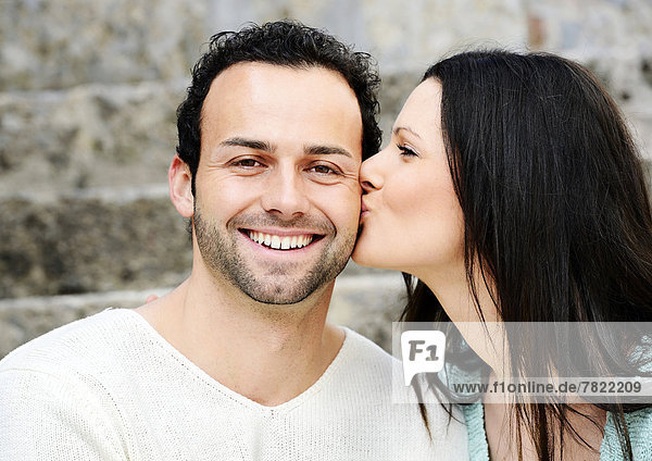 Junge Frau küsst jungen Mann auf die Wange