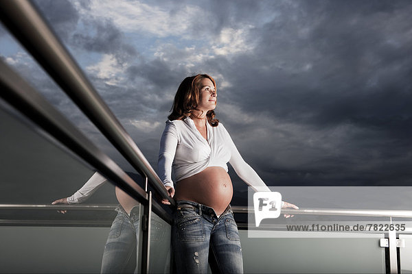 Pregnant woman with a baby bump standing on balcony