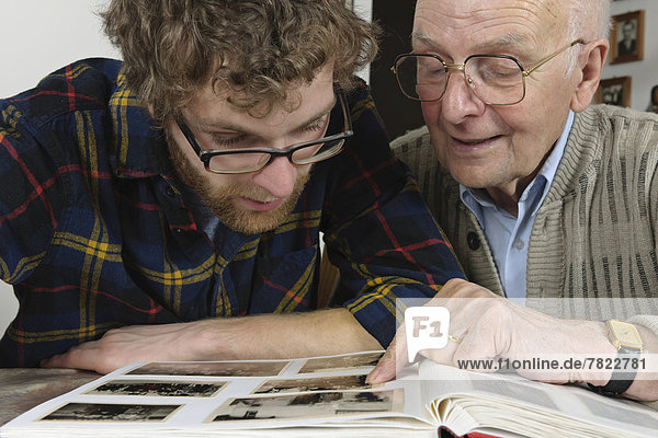 Enkel und Großvater betrachten Fotos in einem Fotoalbum