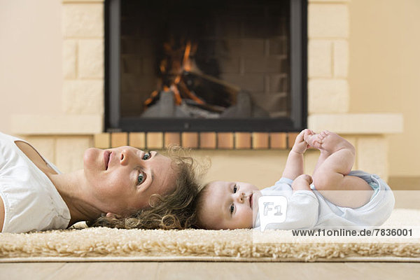 Mutter und Tochter liegen Kopf an Kopf auf einem Teppich vor dem Feuer.