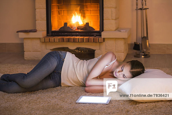 Schöne Frau entspannt sich am Feuer neben dem digitalen Tablett