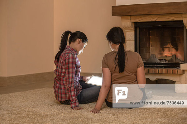 Zwei Frauen  die sich neben dem Feuer entspannen und auf ein digitales Tablett schauen