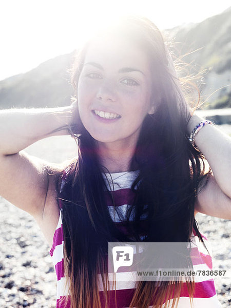 Eine junge Frau lächelt fröhlich am Strand.