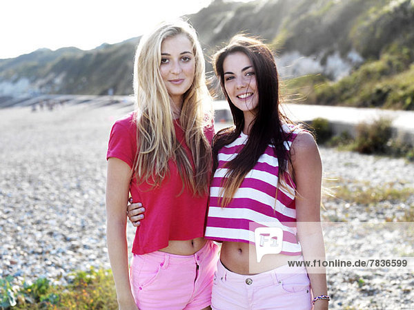 Two smiling young women with their arms around each other standing on a beach