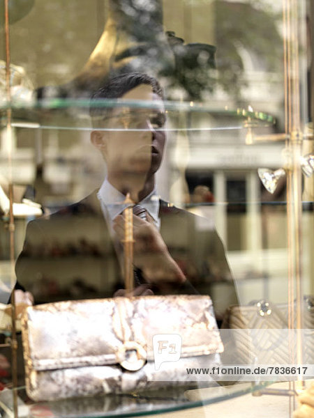 Ein junger Geschäftsmann  der seine Krawatte an einem Schaufenster als Spiegel anpasst.