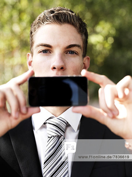 Ein junger Geschäftsmann hält sein Smartphone vor den Mund.