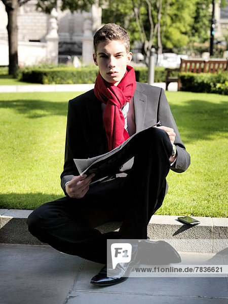 Ein junger Geschäftsmann  der eine Zeitung hält  während er in einem Park sitzt.
