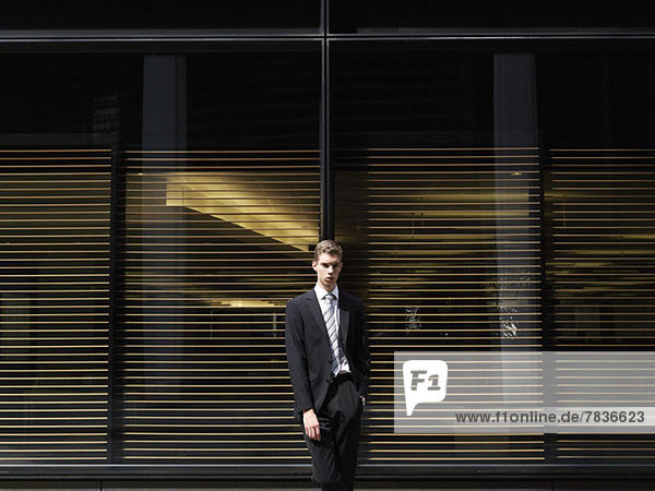 A young businessman leaning against windows with blinds