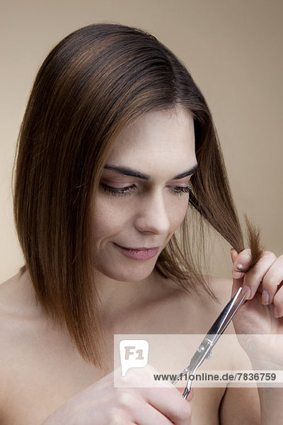 Eine lächelnde junge Frau,  die sich konzentriert,  während sie ihr eigenes Haar schneidet.