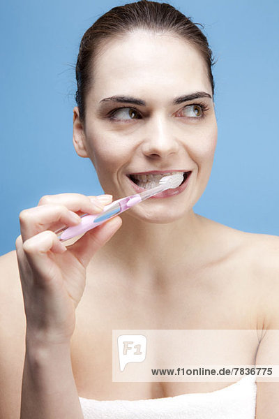 Eine lächelnde junge Frau  die sich die Zähne putzt  während sie nachdenklich wegschaut.
