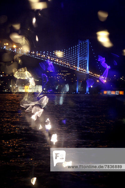 Reflektiertes Licht und Blick auf eine beleuchtete Brücke über Wasser bei Nacht