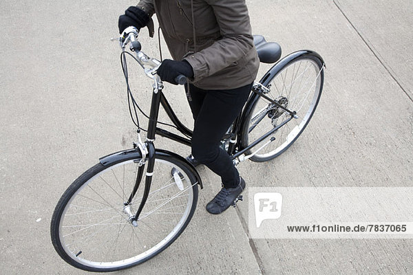 Eine Frau steht mit dem Fahrrad auf dem Bürgersteig.