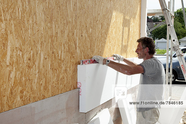Europe,  Germany,  Rhineland Palatinate,  Man sticking polystyrene on wooden house wall