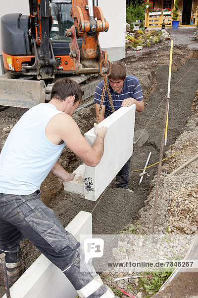 Europe,  Germany,  Rhineland Palatinate,  Men installing corner stone in soil while house building