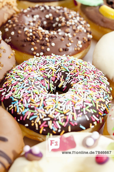 Variety of doughnuts topped with icing and sprinkles,  close up