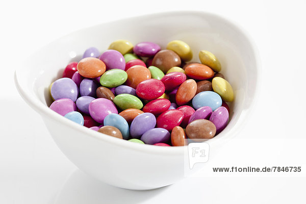 Bowl of chocolate buttons on white background  close up