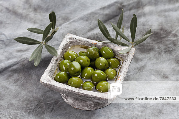 Bowl of green olives in olive oil on textile  close up
