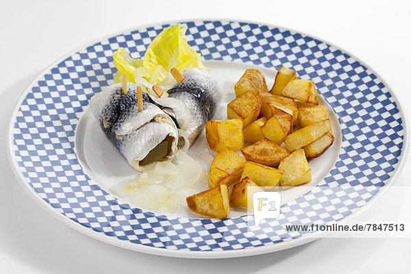 Rollmop herring with roasted potatoes and onions on a plate