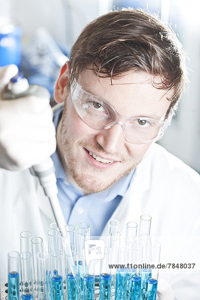 Germany  Young scientist pipetting blue liquid into test tubes  close up