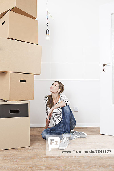 Woman sitting on floor besides stack of cardboard boxes