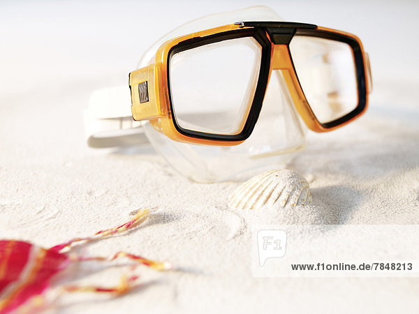 Swimming goggles on sand with shell