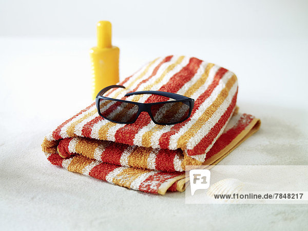 Sunglasses  sunscreen lotion and towel on sand