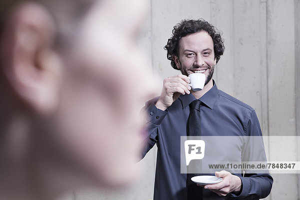 Germany  North Rhine Westphalia  Cologne  Businessman drinking tea while woman in foreground