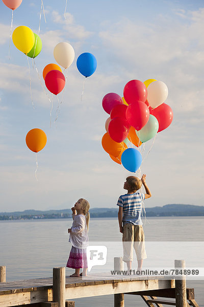 Junge und Mädchen stehen am Pier und fliegen Ballons am Starnberger See.