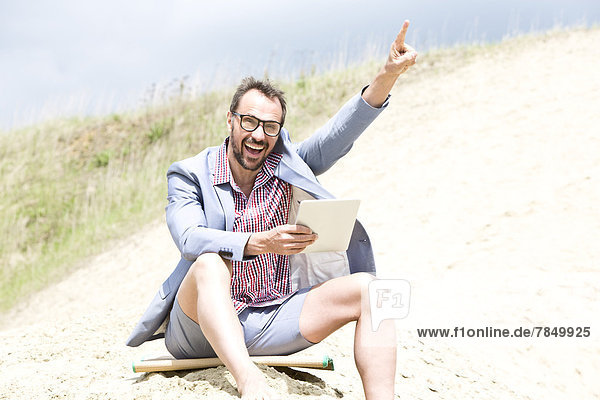 Deutschland  Bayern  Portrait eines Geschäftsmannes auf Sand sitzend mit digitaler Tafel  lächelnd