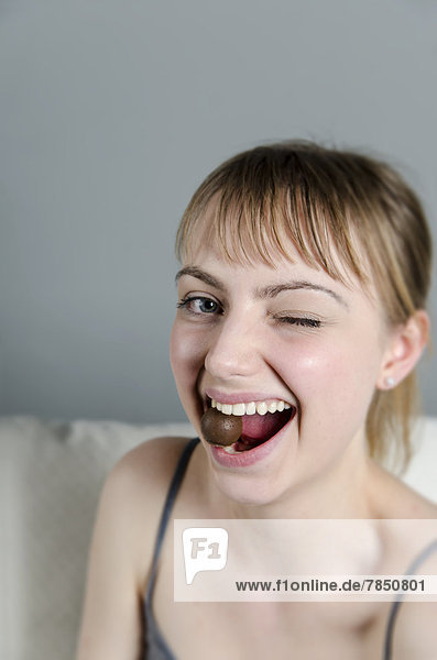 Porträt einer jungen Frau  die Schokoladenpraline isst  lächelnd