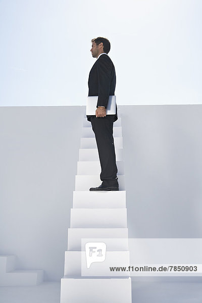 Geschäftsmann im schwarzen Anzug mit Laptop auf der Treppe stehend