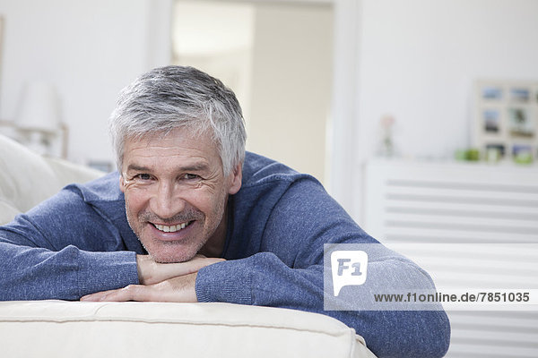 Porträt eines reifen Mannes  der sich auf der Couch entspannt  lächelnd