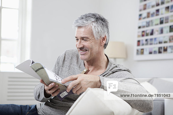 Erwachsener Mann liest Magazin auf der Couch  lächelnd