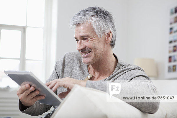 Erwachsener Mann mit digitalem Tablett auf der Couch  lächelnd