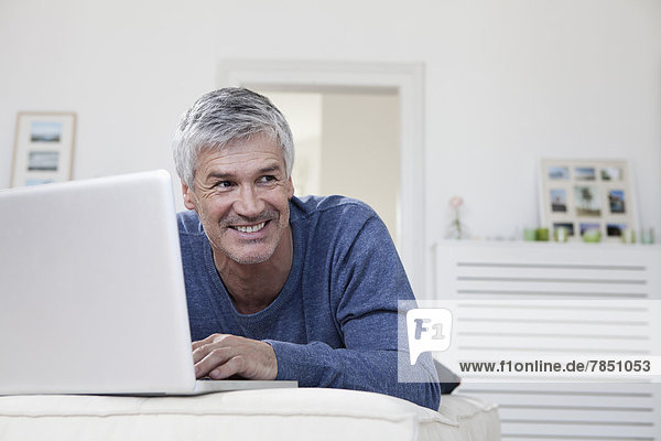 Erwachsener Mann mit Laptop auf der Couch  lächelnd