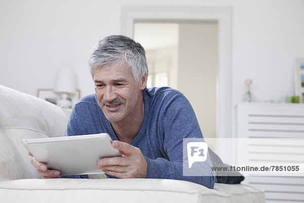 Mature man using digital tablet on couch  smiling