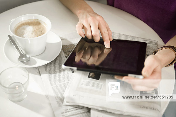 Junge Frau sitzt am Tisch im Café  mit digitalem Tablett