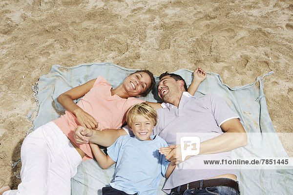 Spain  Family lying on beach at Palma de Mallorca  smiling