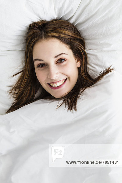 Porträt einer jungen Frau auf dem Bett liegend  lächelnd