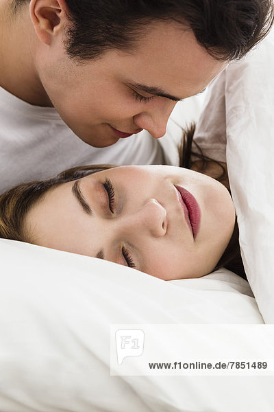 Junger Mann schaut junge Frau im Schlaf an