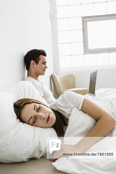 Young woman sleeping while young man using laptop in background