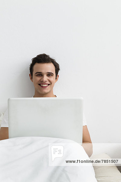 Portrait of young man using laptop  smiling