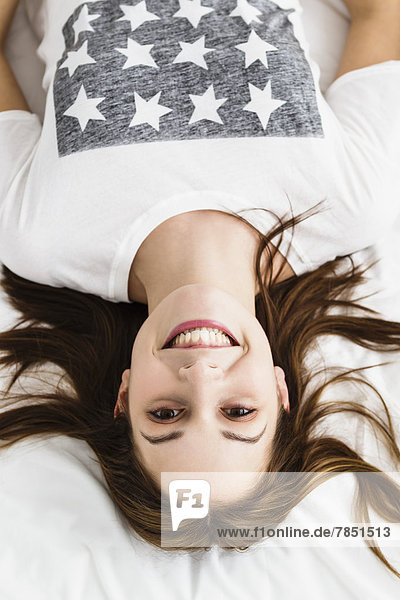 Porträt einer jungen Frau auf dem Bett liegend  lächelnd