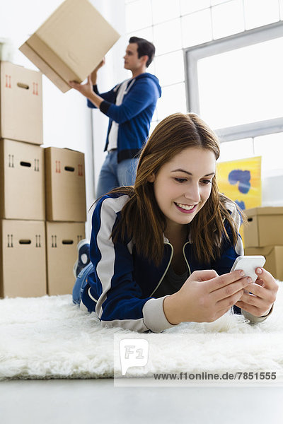 Young woman using mobile phone while man holding box  smiling