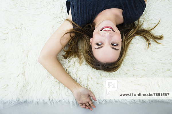 Junge Frau auf dem Teppich liegend  lächelnd