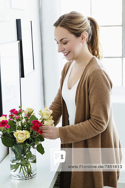 Junge Frau arrangiert Blumen in Vase  lächelnd