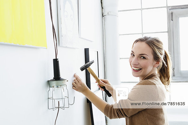 Portrait of young woman hammering wall  smiling